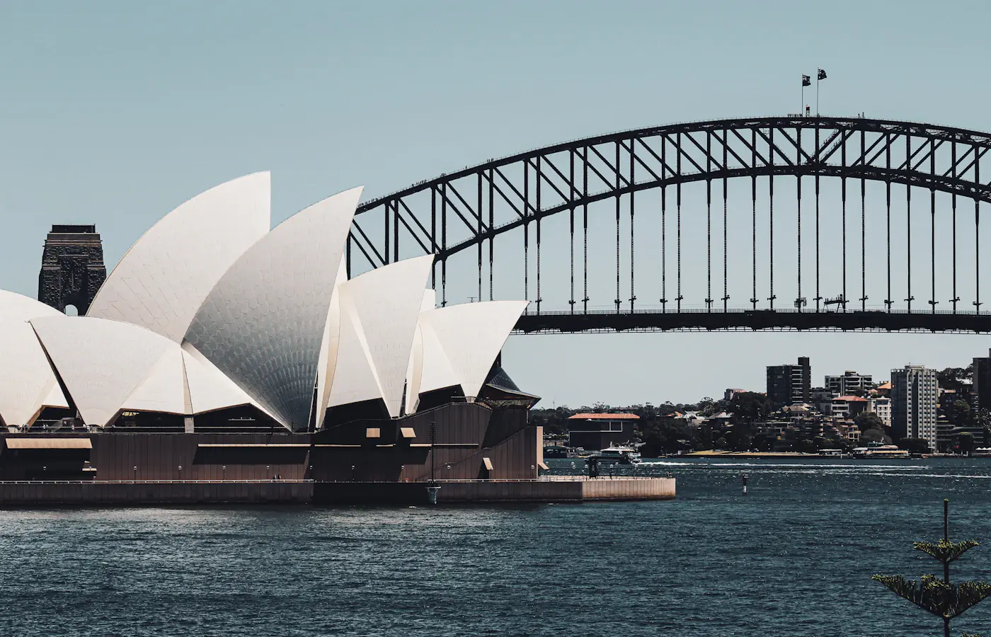 Sydney Opera House beside the harbour with the Sydney Harbour Bridge behind it.