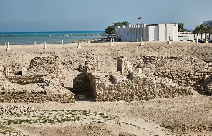 Wykopane kamienne pozostałości w Qal'at al-Bahrain z muzeum stanowiska i morzem w tle