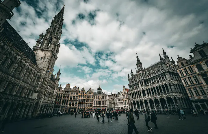 Gabled historic buildings around Grand Place in Brussels beneath a cloudy sky.