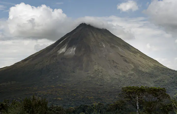 Arenal volcano rising above green forest under scattered clouds in Costa Rica