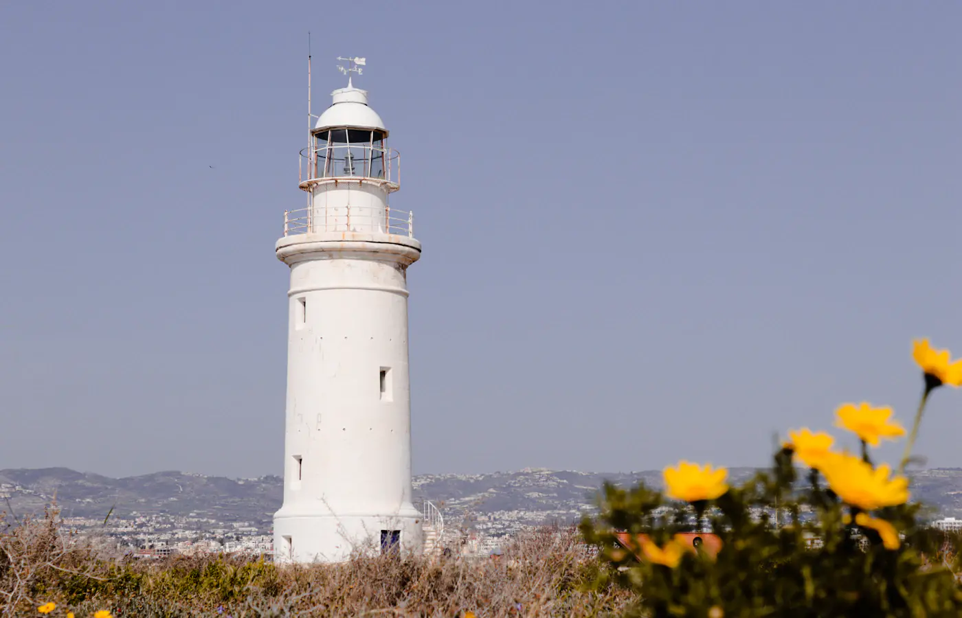 O farol branco de Pafos atrás de flores amarelas em Pafos, Chipre
