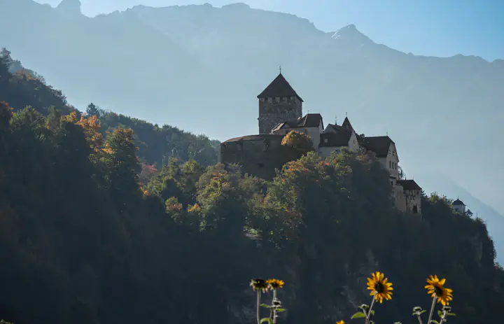 Vaduz Castle above wooded slopes with mountain peaks behind it, in Liechtenstein