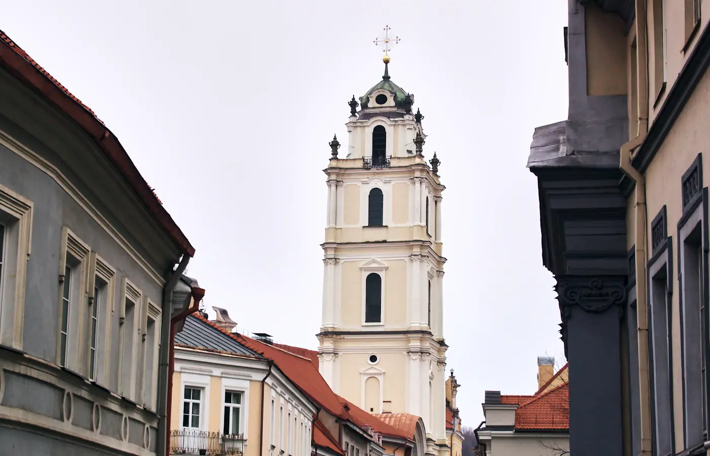 Una torre di chiesa chiara sopra le strade strette e i tetti in tegole di Vilnius.