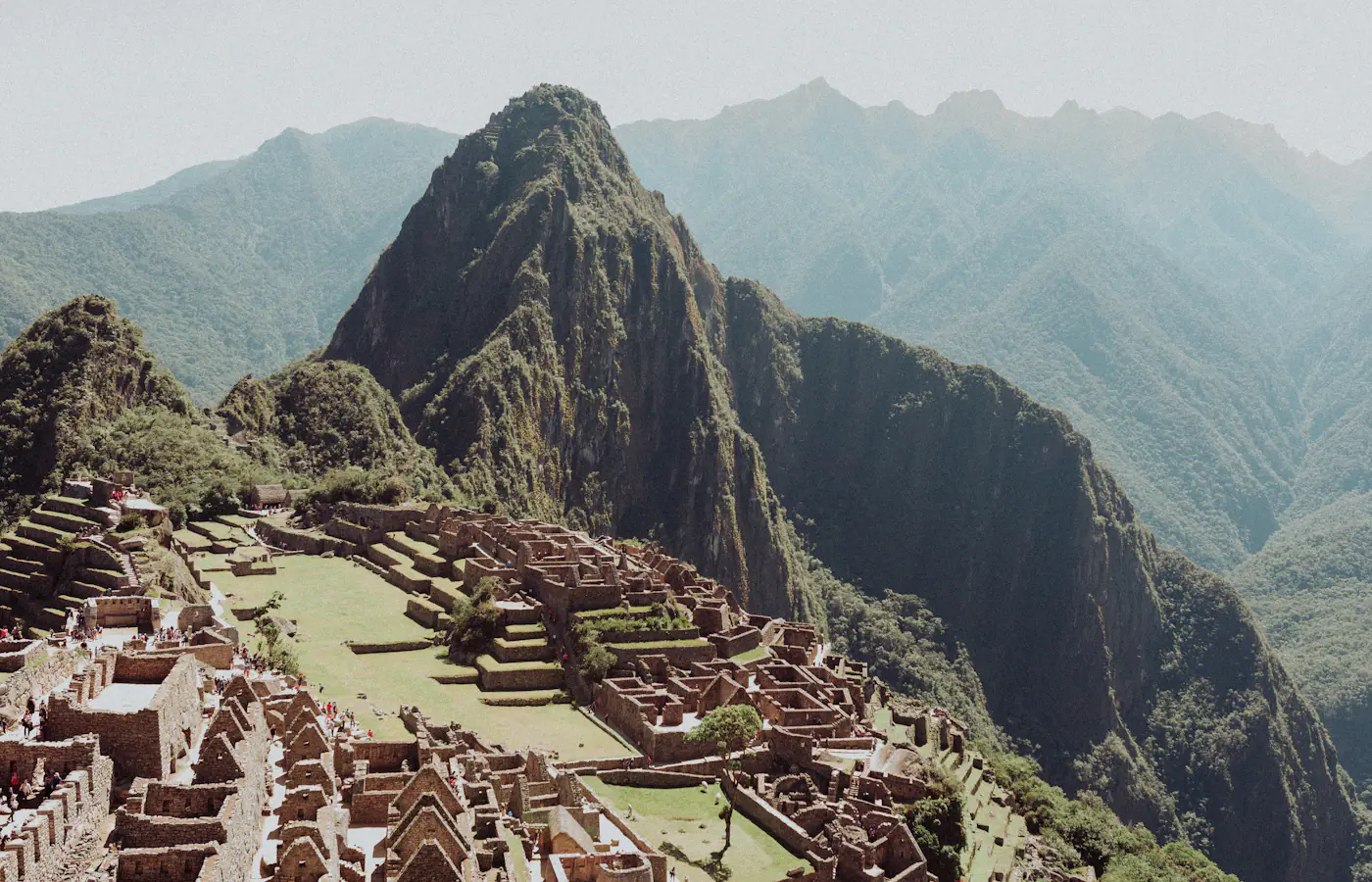 Oude stenen terrassen en muren van Machu Picchu met de steile groene top van Huayna Picchu erachter, Peru