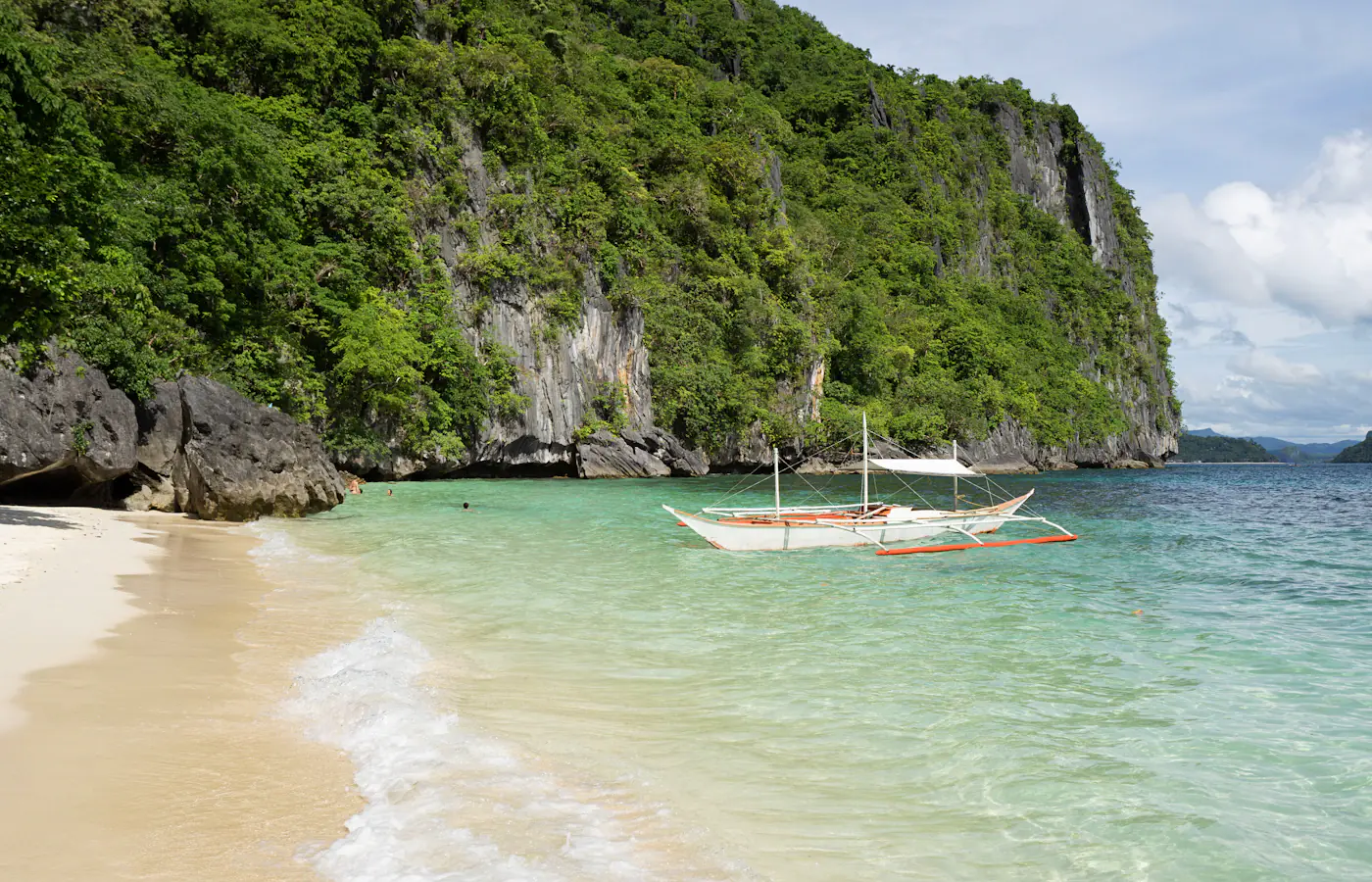 Auslegerboot an einem Strand unter Kalksteinfelsen in El Nido, Palawan