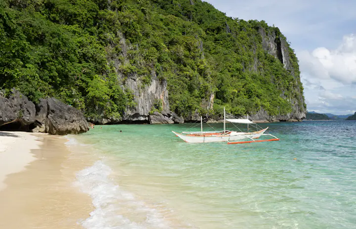 Auslegerboot an einem Strand unter Kalksteinfelsen in El Nido, Palawan